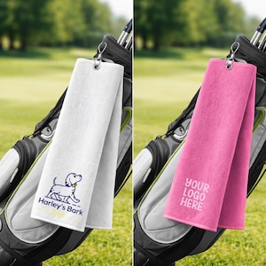 May include: A white golf towel featuring a blue dog illustration and the text Harley's Bark, and a pink golf towel with the text YOUR LOGO HERE. Both towels include a silver metal grommet and a swivel clip for attachment to a golf bag.
