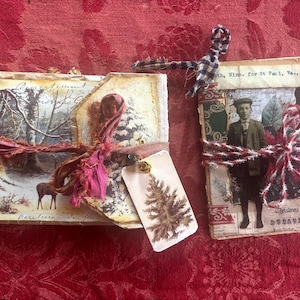 May include: Two vintage-style journals with decorative covers. One features a winter scene with a deer, the other a sepia-toned portrait. Both are tied with ribbon and include tags with Christmas tree illustrations.