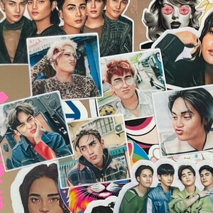 May include: A collection of stickers on a laptop featuring various portraits of people, cartoon characters, and logos. The stickers are diverse in style, including illustrations and photographs, with a mix of colors and designs.
