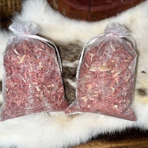 Op de afbeelding: Twee kleine witte gaaszakjes gevuld met roze en witte houtsnippers. De zakjes liggen op een wit, pluche oppervlak.