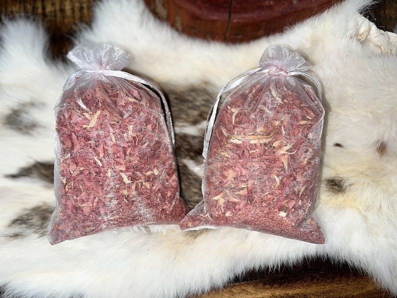 Op de afbeelding: Twee kleine witte gaaszakjes gevuld met roze en witte houtsnippers. De zakjes liggen op een wit, pluche oppervlak.