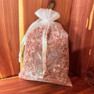 Op de afbeelding: Een witte gaas zak gevuld met cederhouten spaanders. De zak is vastgebonden met een wit lint en ligt op een houten oppervlak.