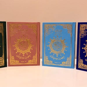 May include: Four hardcover books with gold foil Arabic calligraphy and intricate geometric patterns on the covers. The books are colored dark green, dusty rose, light blue, and royal blue, each featuring identical ornate gold decorative borders.