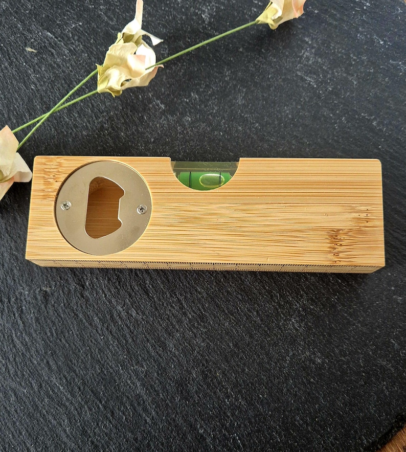 May include: A wooden bottle opener with a built-in level. The opener is made of light brown bamboo and has a silver metal bottle opener.