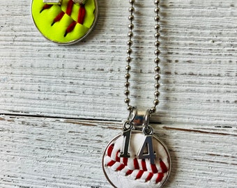 May include: Two silver necklaces with softball charms. One charm is yellow with red stitching and the number 20. The other charm is white with red stitching and the number 14.