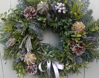 May include: A festive Christmas wreath with a mix of greenery, pinecones, and gold ornaments. The wreath features a silver ribbon and is displayed on a light green door, creating a welcoming holiday decoration.