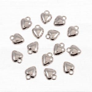 May include: A collection of 16 silver heart-shaped charms with a loop at the top. The charms are scattered on a white surface.