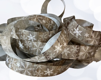 May include: A spool of brown ribbon with a white snowflake pattern. The ribbon is made of a soft, textured fabric and is perfect for adding a touch of winter cheer to your crafts and gifts.