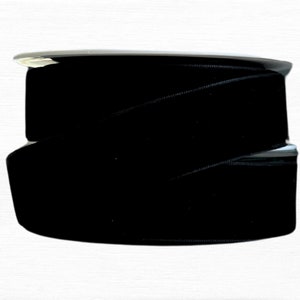May include: A spool of black velvet ribbon. The ribbon is wound tightly and has a slight sheen.
