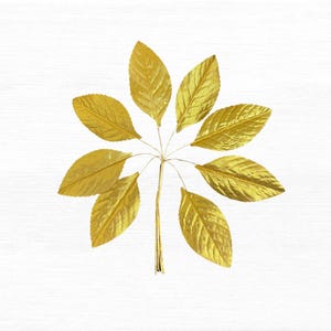 May include: A decorative arrangement of eight gold leaves, each with a textured finish, radiating from a central stem. The leaves are attached to the stem with fine wire. The background is a white, textured surface.
