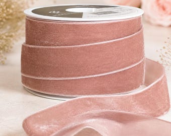 May include: A spool of dusty rose velvet ribbon with a smooth, soft texture. The ribbon is wound tightly around a white plastic core, with a single length of the fabric extending outward from the base, showcasing its consistent color and sheen.