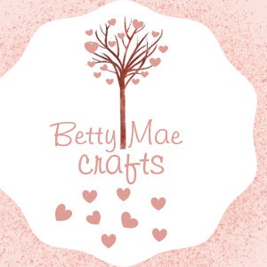 May include: A banner with a pink watercolor background and gold accents. The text reads "Handmade Cards For All Occasions" and "Craft Supplies For All Types of Crafts". The center features a logo with the text "Betty Mae crafts" and a tree design.