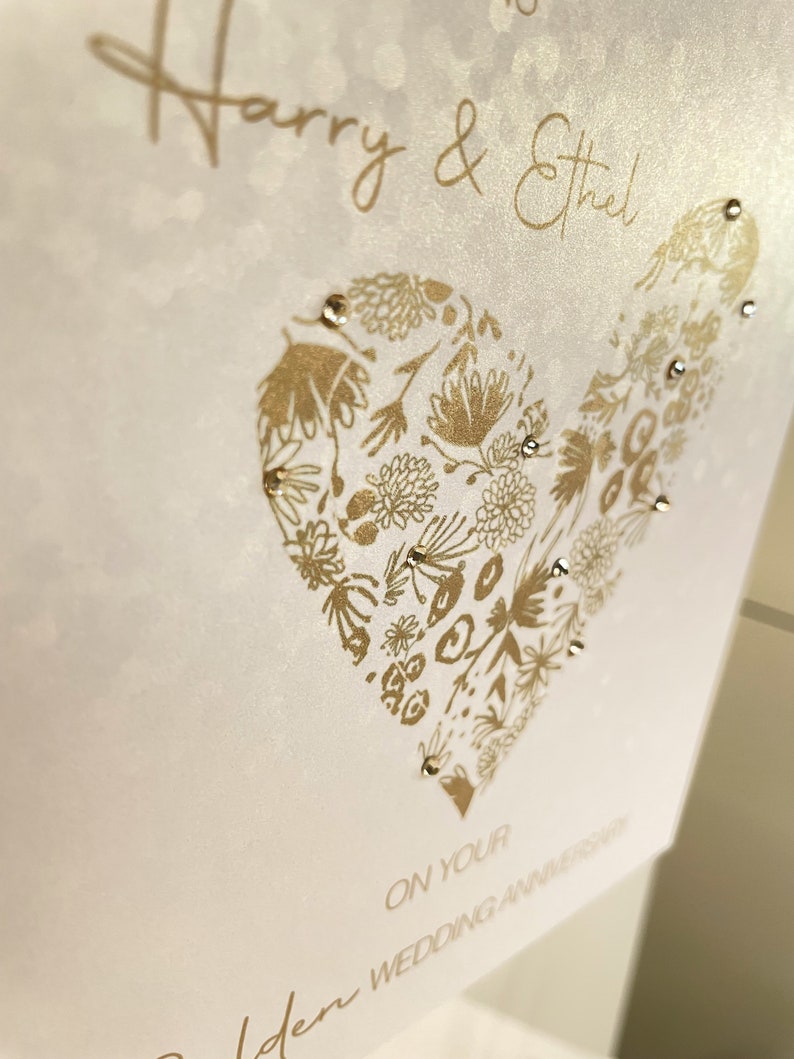 Golden Wedding Anniversary card printed on sequin-effect pearlescent card, featuring a floral gold heart design and personalised names, hand finished with sparkling gold diamantes.