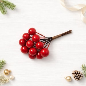 May include: A small decorative cluster of glossy red berries attached to thin brown wire stems. The berries are round and smooth, gathered together at the base with a brown paper-wrapped binding, creating a compact, uniform bunch of artificial fruit.