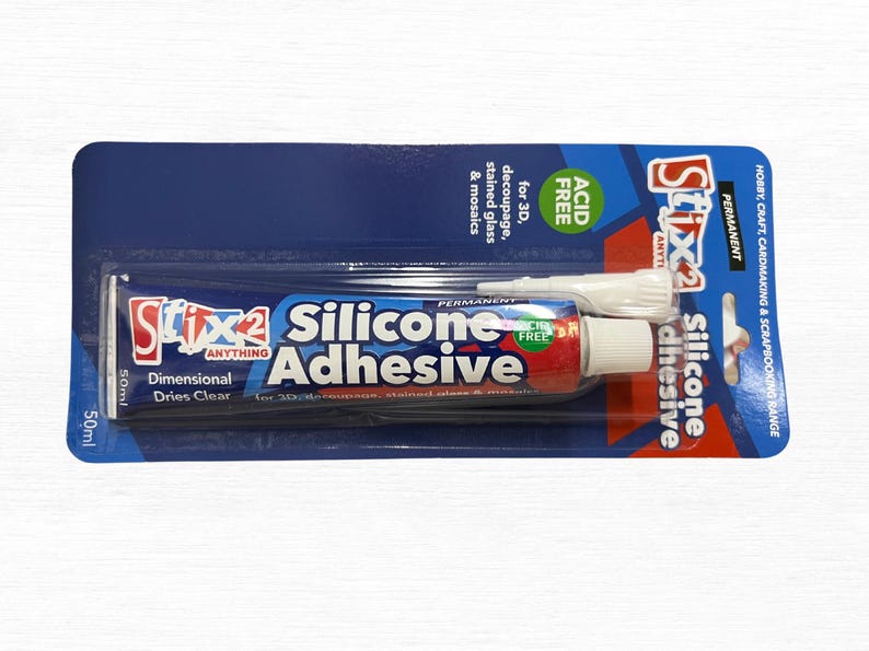 May include: A tube of Stix2 Silicone Adhesive, 50ml, on a blue and white card. The tube is red, white, and blue with the words "Silicone Adhesive" prominently displayed. The packaging indicates it's acid-free and suitable for 3D decoupage, stained glass, and mosaics.