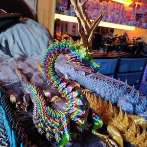 Puede incluir: Una figurita de dragón iridiscente multicolor con cuernos de oro. El dragón está enroscado con la cola envuelta alrededor de su cuerpo. La figurita está hecha de un material brillante y metálico.