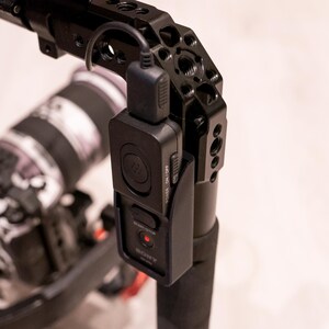 Puede incluir: Plataforma de c&aacute;mara negra con un m&oacute;dulo de control negro adjunto. El m&oacute;dulo tiene una luz roja y la palabra "SONY" impresa. La plataforma est&aacute; montada sobre una superficie blanca. El objetivo de la c&aacute;mara es visible en el fondo.
