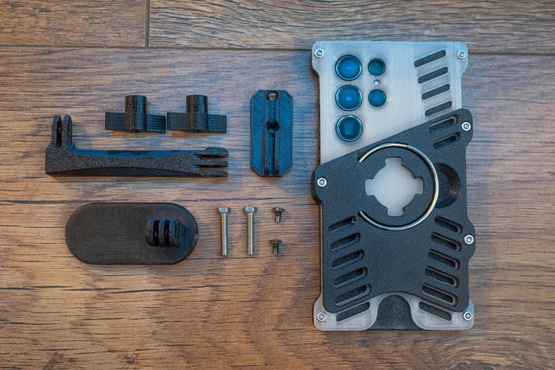 May include: A black and silver phone case with a built-in camera lens and a ring holder. The case comes with a variety of accessories, including a phone mount, screws, and a small black piece with a GoPro mount.