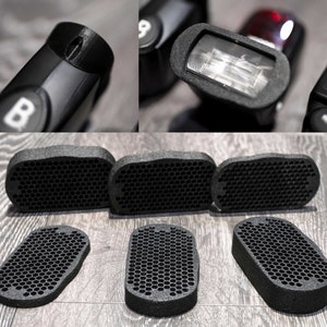 May include: Five black honeycomb-shaped foam light diffusers for a flash. The diffusers are designed to soften the light from a flash and create a more natural look.