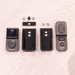 Puede incluir: Un conjunto de dispositivos y accesorios electr&oacute;nicos negros y grises, que incluyen un peque&ntilde;o dispositivo con pantalla etiquetado como "RONIN", dos fundas protectoras negras, un mando a distancia "SONY" y varios tornillos.
