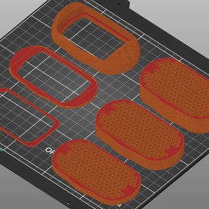 May include: Five 3D printed objects on a black grid surface. Four of the objects are rectangular frames with rounded corners. One object is a solid, oval-shaped object with a honeycomb pattern.
