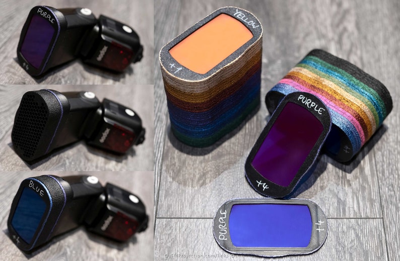 May include: Three flash units with different colored gels attached. The gels are purple, blue, and yellow. The flash units are black with a red button on the side. The gels are labeled with the color and a +1.
