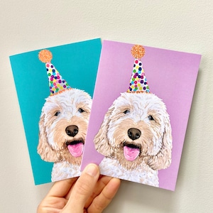 May include: Two greeting cards showing a smiling dog wearing a party hat. One card has a turquoise background, the other a lilac background. The dog has a light brown coat, a pink tongue, and a black nose. The party hats are white with colourful polka dots and an orange pom-pom.