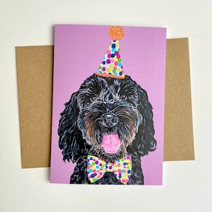 May include: A birthday card with a black dog wearing a party hat and bow tie. The dog has a pink tongue and is set against a lilac background. A brown envelope is included.
