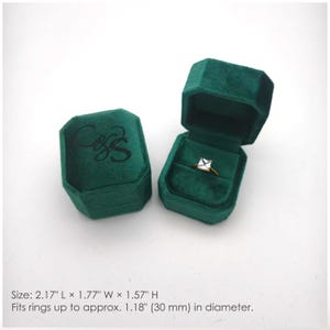 May include: Two dark green velvet ring boxes with a hexagonal shape. One box is closed with a black script logo on top, and the other is open, containing a gold ring with a square stone. Dimensions are 2.17 inches L by 1.77 inches W by 1.57 inches H.