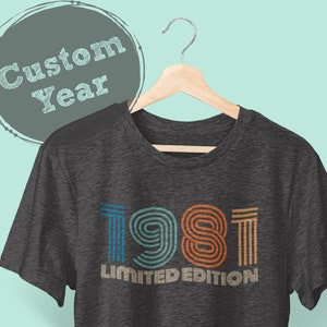 May include: A dark gray t-shirt with a vintage-style graphic that says "1981 Limited Edition". The graphic is in rainbow colors.