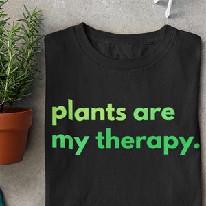 Puede incluir: Camiseta negra con texto verde que dice "plants are my therapy."