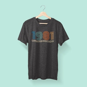 May include: A dark grey t-shirt with a vintage-style graphic of the year 1981 in colorful stripes. The text "LIMITED EDITION" is printed below the year.