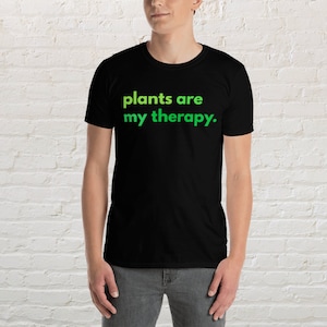 Puede incluir: Una camiseta negra con el texto "plants are my therapy." impreso en verde.