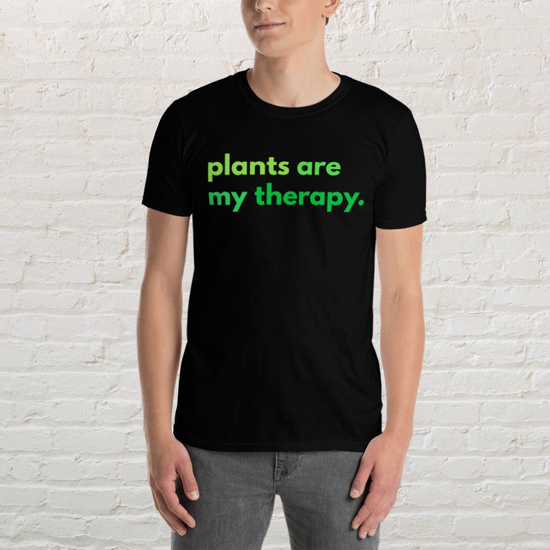 Puede incluir: Una camiseta negra con el texto "plants are my therapy." impreso en verde.