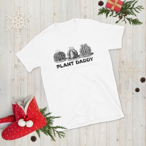 May include: White t-shirt with a black and white illustration of three cacti and the text "PLANT DADDY" printed on the front.
