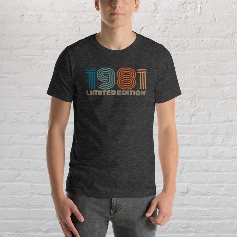 May include: A dark heather grey t-shirt with a vintage-style graphic of the year 1981 in colorful stripes. The text "LIMITED EDITION" is printed below the year.