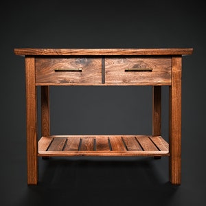 Op de afbeelding: Een donkerbruine houten bijzettafel met twee laden en een onderplank. De laden hebben messing handgrepen.