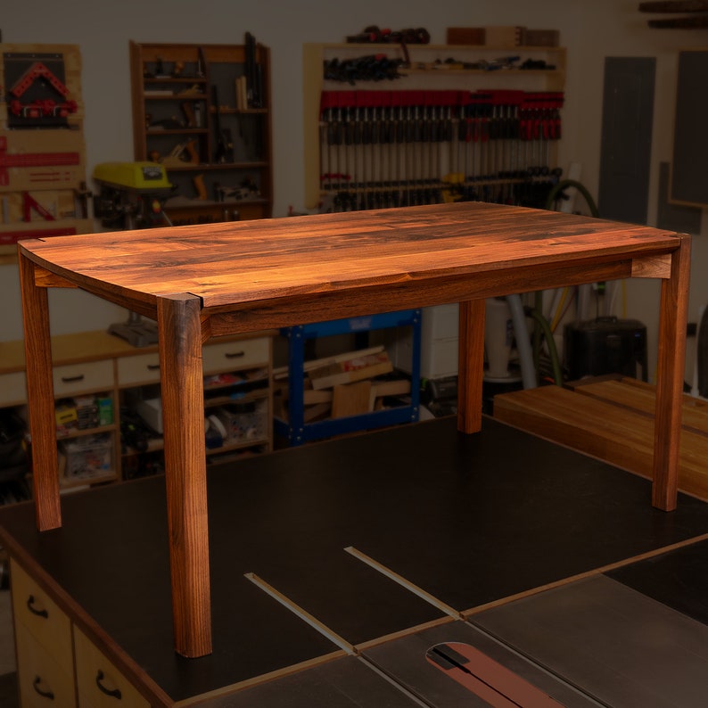May include: A solid wood dining table with a dark brown finish and a rectangular top. The table has four legs and is made of a sturdy wood.