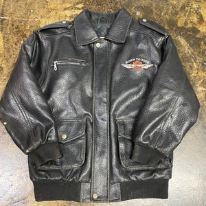 May include: A black leather jacket featuring a collared neckline, long sleeves with ribbed cuffs, and a ribbed hem. The front includes a zippered chest pocket, two snap-button flap pockets, and a Harley-Davidson logo with the text BORN TO RIDE.
