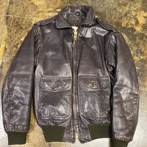 Può includere: Un giubbotto bomber in pelle marrone scuro con chiusura frontale a zip, colletto ripiegato, due tasche frontali con patta e chiusura a bottone, polsini e fascia in vita in maglia a coste di colore verde oliva scuro.