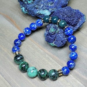 May include: A blue and green gemstone bracelet with gold accents. The bracelet is made with round beads and has a stretchy band.