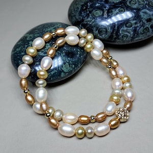 May include: A double strand pearl necklace with gold accents and a gold clasp. The pearls are white, cream, and gold in color.