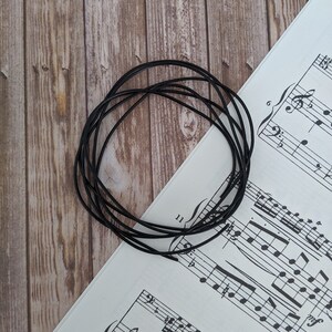May include: A close-up of a black elastic cord, coiled in a circle, on a white sheet of music with black musical notes.