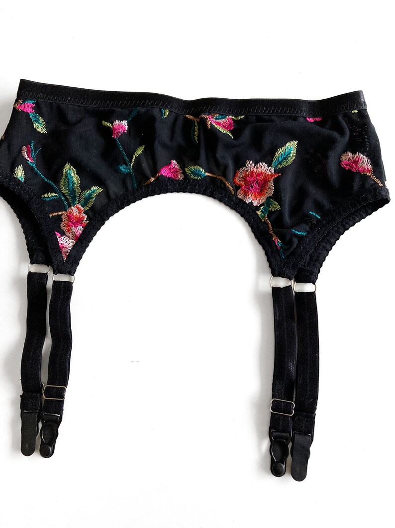 May include: Black garter belt with floral embroidery and adjustable straps. The straps have metal clips.