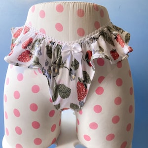 Puede incluir: Ropa interior blanca con un top con volantes y un estampado de fresas. La ropa interior está sobre un fondo blanco con lunares rosas.