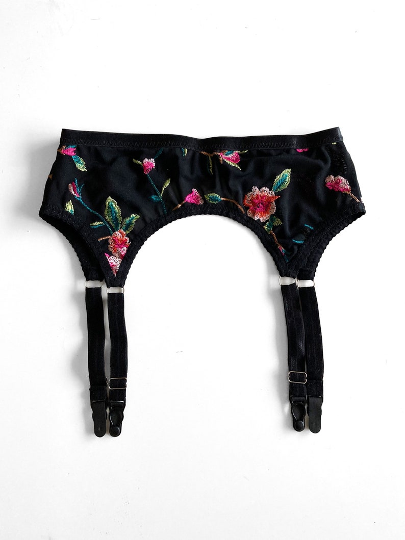 May include: Black garter belt with floral embroidery. The belt has two adjustable straps with metal clips.