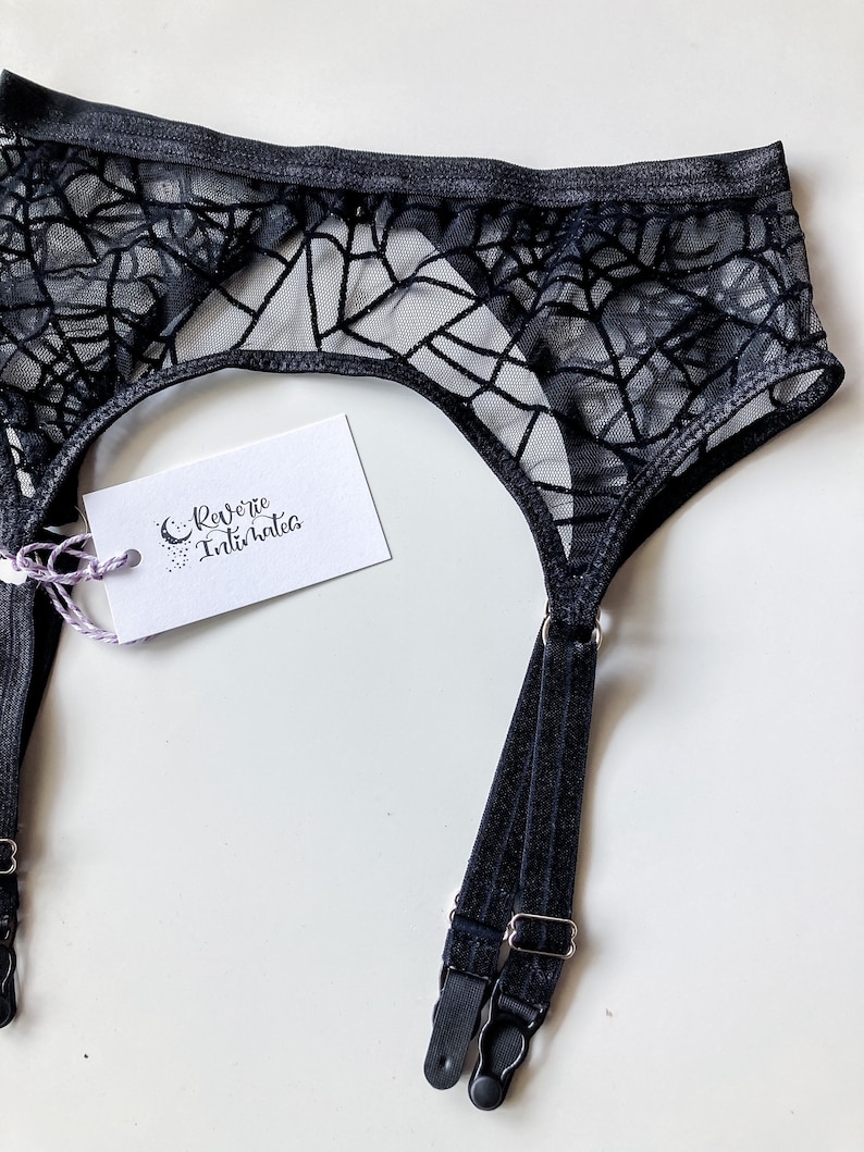 Puede incluir: Ligero de liga negro con un dise&ntilde;o de telara&ntilde;a. El liguero tiene dos correas ajustables con cierres plateados. La etiqueta dice "Reverie Intimates".