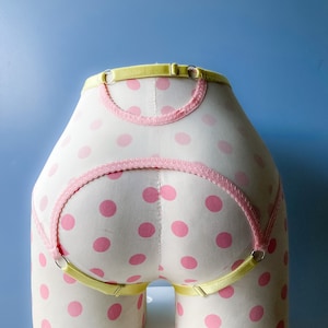May include: Yellow and pink polka dot suspender belt with adjustable straps. The suspender belt is made of a soft, stretchy material and has a delicate lace trim.