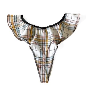 Puede incluir: Un tanga blanco y rosa a cuadros con ribete negro y una parte superior con volantes.