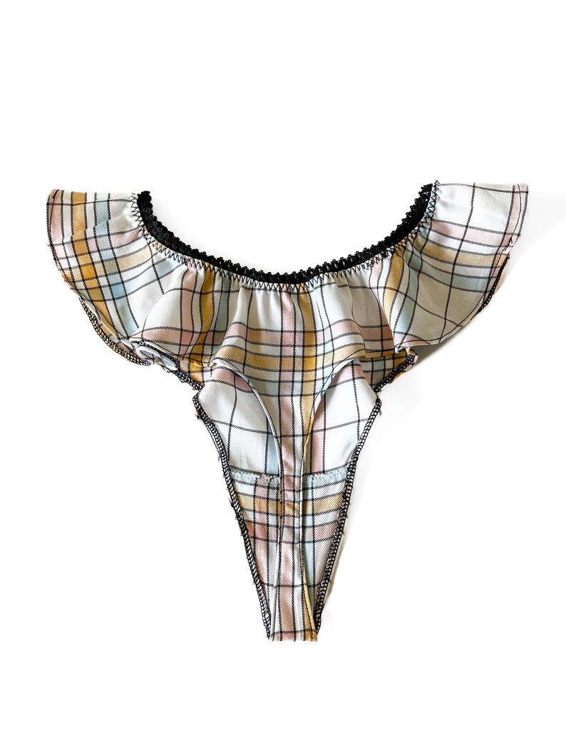 Puede incluir: Un tanga blanco y rosa a cuadros con ribete negro y una parte superior con volantes.